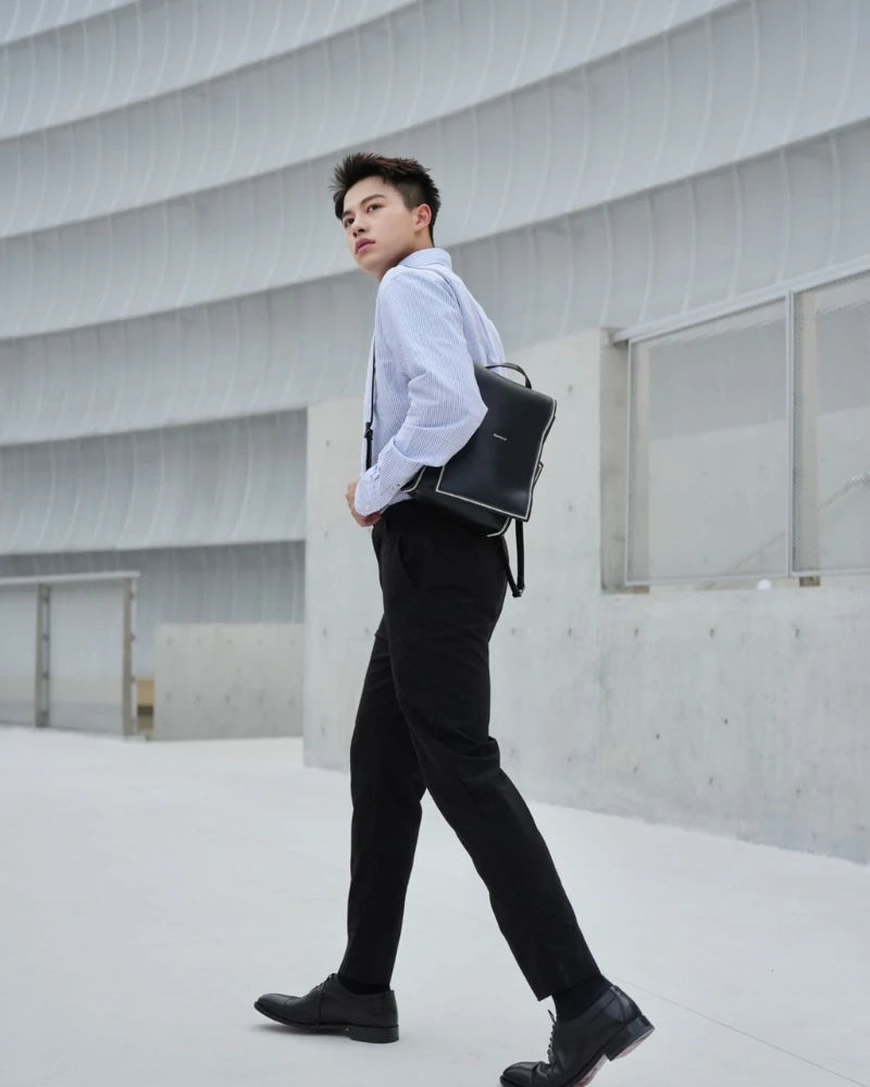 A male model wearing the Somlord 2-in-1 Convertible Leather Mini Backpack while walking in an urban architectural setting, showcasing the bag's professional and modern aesthetic for daily commutes.