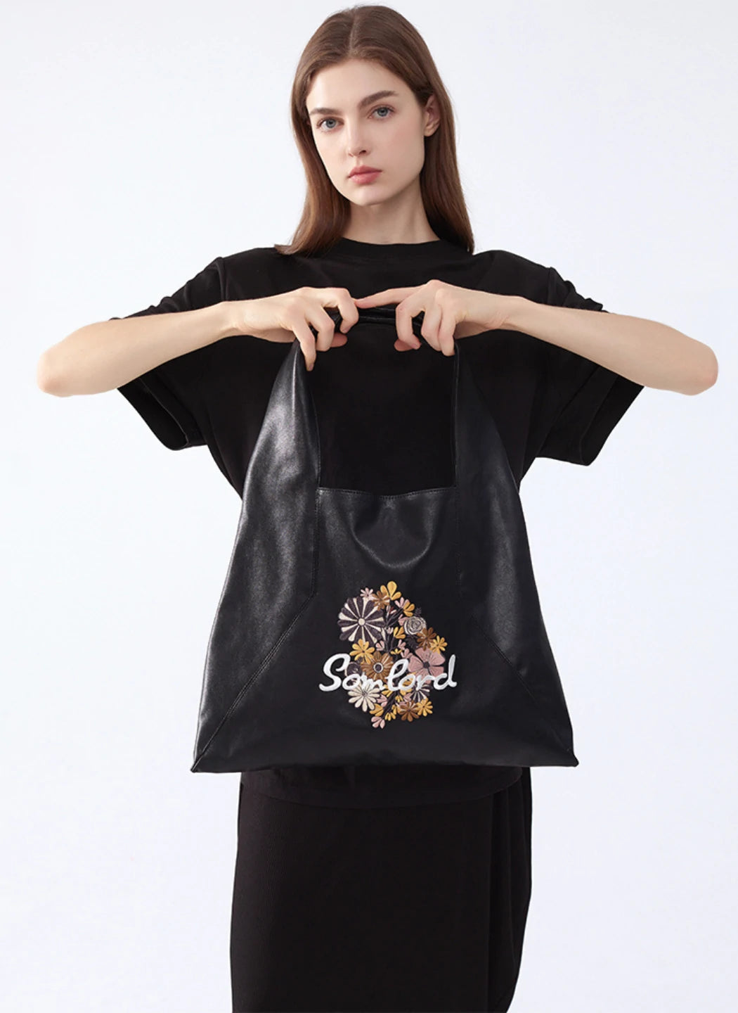 A model holding the Somlord Artistic Embroidered Triangle Soft Leather Tote Bag, featuring intricate floral embroidery and a sleek triangle design, ideal for modern casual and travel looks.