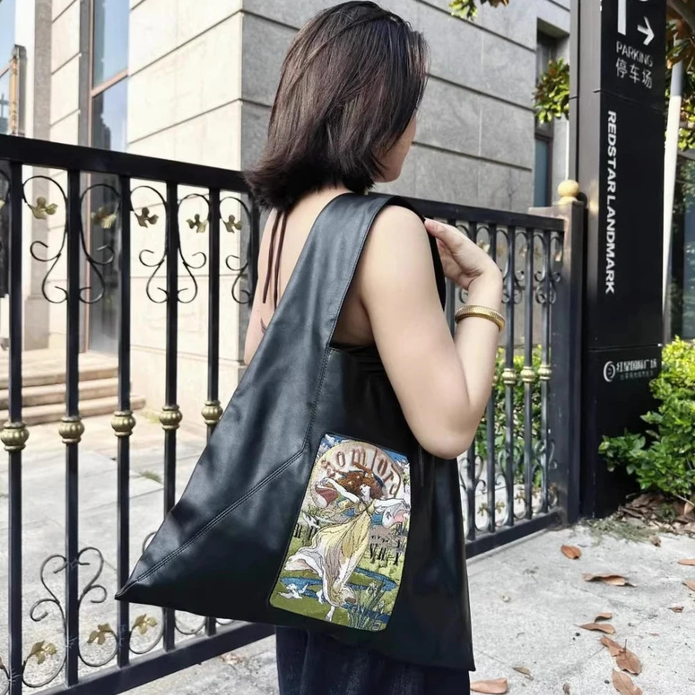 In front of a European-style building, the model carries the Somlord Artistic Embroidered Triangle Soft Leather Tote Bag with Goddess embroidery design. The detailed stitching and soft leather material radiate sophistication and luxury.