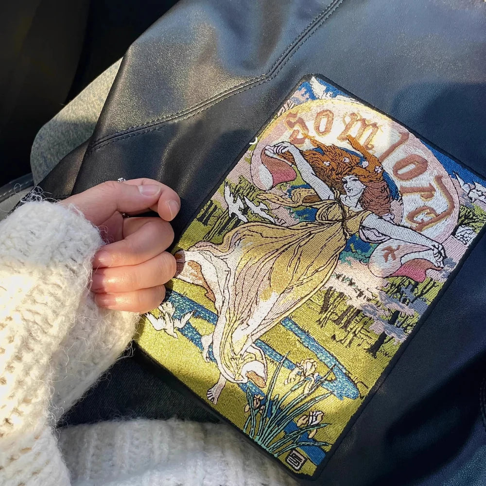 A detailed close-up captures the Goddess embroidery design on the Somlord Artistic Embroidered Triangle Soft Leather Tote Bag. The golden hues and artistic patterns stand out against the smooth leather surface.