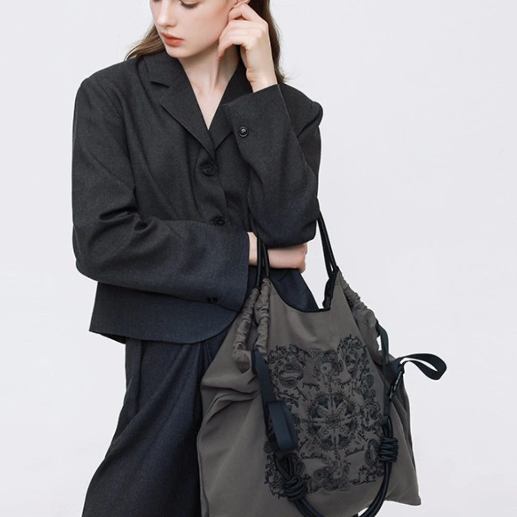 A professional model in a dark gray suit holding a Somlord embroidered tote bag, featuring intricate floral patterns and minimalist elegance, ideal for business or casual settings.