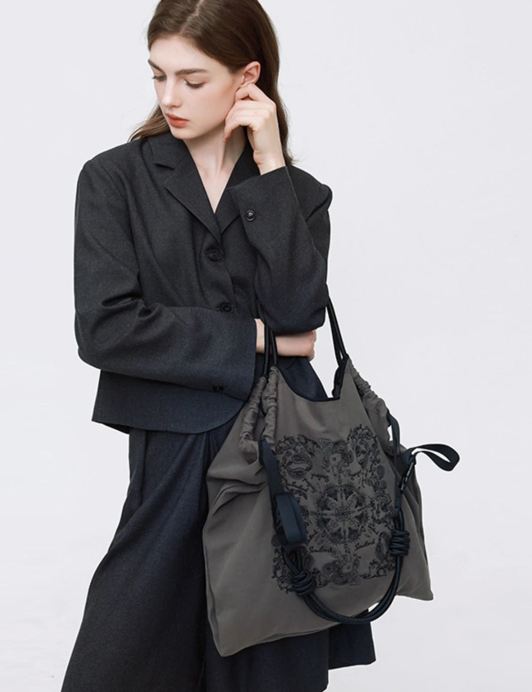 A professional model in a dark gray suit holding a Somlord embroidered tote bag, featuring intricate floral patterns and minimalist elegance, ideal for business or casual settings.