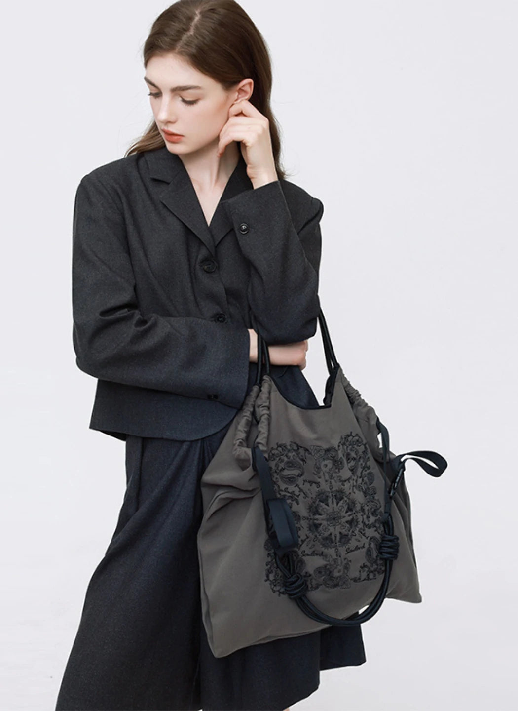 A professional model in a dark gray suit holding a Somlord embroidered tote bag, featuring intricate floral patterns and minimalist elegance, ideal for business or casual settings.