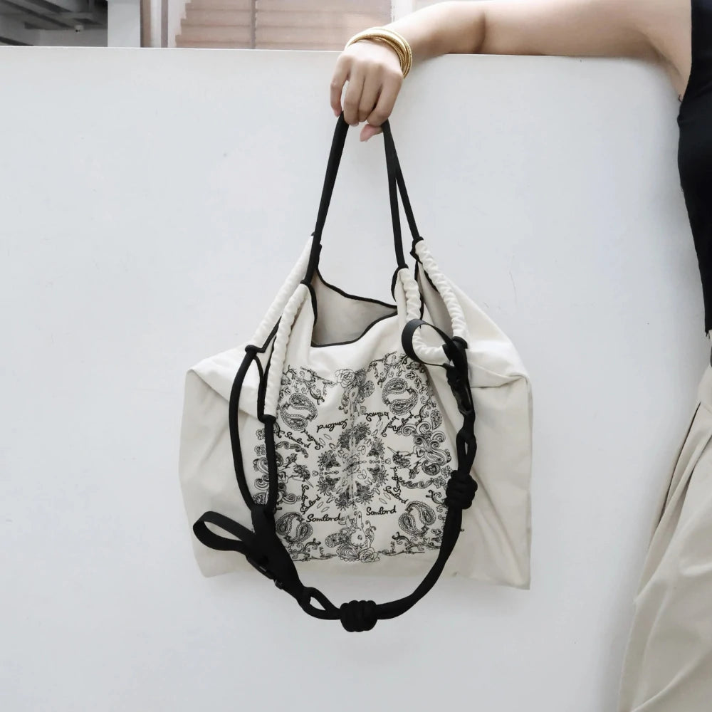 omlord Paisley Embroidered Crossbody Tote Bag in soft beige, featuring intricate paisley embroidery and adjustable black drawstring handles, ideal for urban chic style.