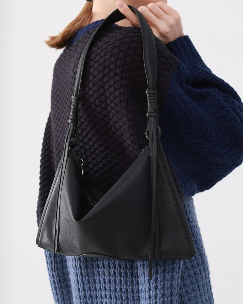 Close-up of a stylish black Somlord shoulder bag with leather straps, held by a model wearing a cozy navy-blue sweater, highlighting the bag's minimalist design and high-quality craftsmanship.