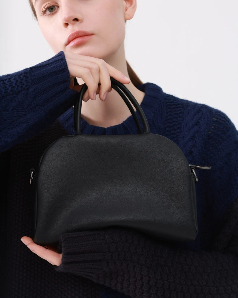 A compact black leather Somlord handbag held elegantly by a model in a navy sweater, featuring clean lines and a structured silhouette, perfect for modern city lifestyles.